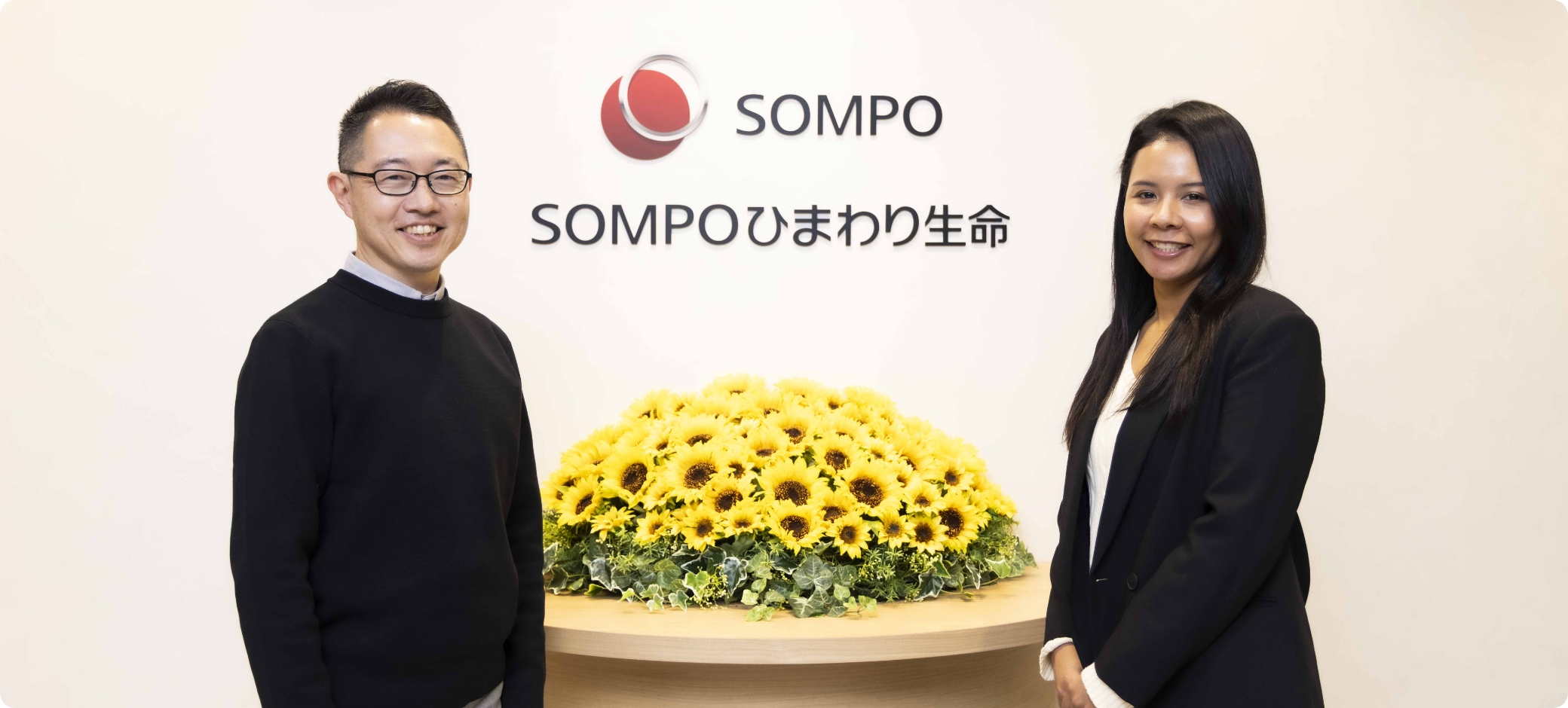 記事のサムネイル。SOMPOひまわり生命のロゴの前で男性と女性がカメラに目線を送っている。